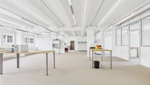 Empty office room with desks and fluorescent ceiling lights, carpeted floor