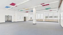 Empty room with gray carpeted floor, white walls, two sets of double doors, large windows, central pillar