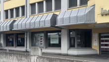 2 story building, yellow wall, grey roof, entrance with metal railings, glass windows, large awnings