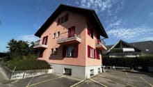 2-story residential building with a pink exterior, balconies, and a parking area in the front.