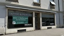 Storefront for tattoo and piercing studio with sign, windows and door visible.