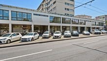 White commercial building with glass facades and several vehicles parked in front