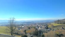 top view of a neighborhood with houses, mountains, and wide valley, rooftops, trees and a road in between