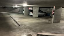 Underground parking garage with concrete walls and floor, several parked cars visible