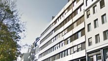 Multi-story building, white exterior, multiple windows, commercial space on the ground floor, trees in the vicinity