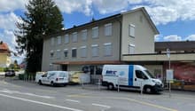 3 story building, grey exterior, multiple windows, awning, 2 vans parked in front