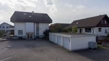 Two houses with garage in the middle. Wide empty space in front.