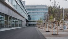 Multi-story office building with glass facade, surrounded by a paved outdoor area with benches and trees