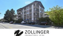 3-story building, grey concrete, multiple windows, parking spaces in front