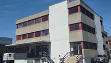 3-story commercial building, modern architectural design, multiple windows, stairs leading to the entrance, parking lot in front, adjacent building in the background