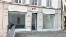 Facade of a building with glass windows and doors, a sign reading 'Joker Personal AG', and a cobblestone pavement in front.