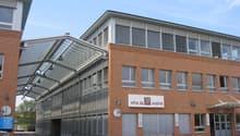 The image shows a multi-story commercial building with a brick facade and large windows. The building has a prominent sign that says 'Vina sa weine', indicating it is likely a wine-related business or facility. The building also has a covered walkway or e