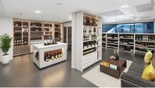 Large, well-lit wine store with extensive shelving and display of wine bottles and glasses. Central display island with additional wine storage. Large windows provide natural light. Variety of wine types and brands available for purchase.