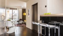 Modern open kitchen with bar stools, white table, white chair, lamp, carpet, couch, and view outside