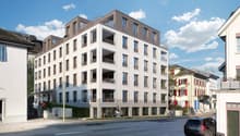 Residential apartment building, modern architecture, multiple floors, balconies, ground floor commercial spaces, and a parking area.
