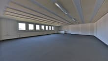 Large open office space with high ceilings, multiple windows, and a carpeted floor. The room appears to be empty and ready for use.