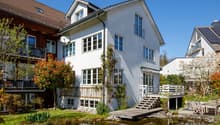 2 story house, white exterior, brown roof, large windows, wooden deck, small pond, garden