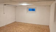 unfinished room with white walls, unfinished ceiling with cracks, small window, unfinished floor with plywood