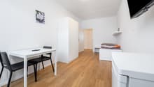 small room with a desk, two chairs, a bed, a wardrobe, a shelf, a television, and a washing machine