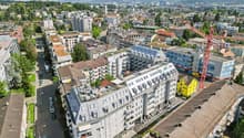 Aerial view of multiple residential buildings, some with rooftop terraces, gray roofs, street with cars, city view