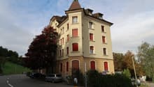 3 story building, beige exterior, red shutters, tower, cars parked in front