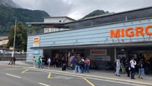 Front entrance of the Migros store with glass walls and doors, many people are entering