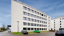 White modern office building, large windows, street lights, parking lot with multiple cars parked