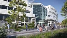 modern office building, glass facade, multiple floors, entrance with canopy, people walking, greenery, bicycle rider