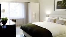 modern bedroom with a king size bed, white walls, large window, white cabinet, desk, white linens, plants