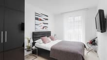 Modern design with white walls, black furniture, double bed, bedside tables with lamps, TV, painting, nightstand with candle and flower vase