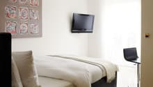 single bed, modern design, mounted TV, decorative painting, white pillow, black cushioned chair