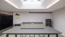 Empty kitchen area with a long table, stools, countertop, sink, and a refrigerator.
