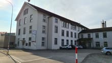 3 story building, white exterior, multiple windows, brown roof, parking lot, cars parked