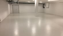 Empty room with white walls and floor, two doors, and pipes on the ceiling