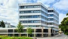 Modern office building, multiple floors, glass windows, metallic façade, greenery around