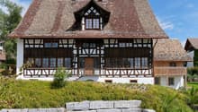 2 story house, brown roof, white and brown wooden facade, wooden balcony, chimneys, large windows