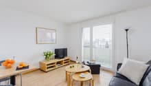 Bright and spacious living room with hardwood floors, white walls, large windows, TV stand, coffee table, and sofa