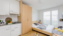 small kitchen area with appliances and utensils, wooden bed, wooden flooring, double window, sink