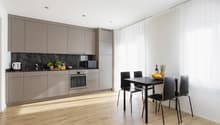 Modern kitchen with wood flooring, gray cabinets, oven, wooden dining table with chairs, bowl of fruit, bottle, glasses