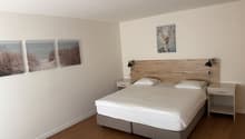 Bedroom with a double bed, two nightstands, and three wall paintings. The bed has white sheets and pillows. The nightstands have drawers and lamps.