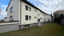 Modern apartment building, white exterior, multiple windows, green lawn in front, pathway leading to entrance