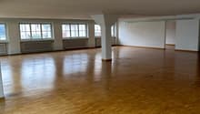 Large open space with hardwood flooring, multiple windows, and white walls. The room appears to be empty and suitable for various purposes such as an office, studio, or event space.