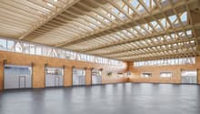 Large open space, metal gray doors, wooden trusses on ceiling, glass windows, brown walls, concrete floor