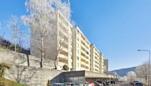 Multi-story apartment building with a parking lot in front, surrounded by trees covered in snow
