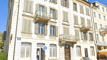 A multi-story building with a classical architectural style, featuring ornate facades, balconies, and large windows. The building appears to house a cafe or restaurant on the ground floor.