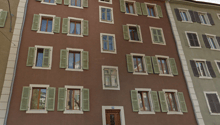 3 story building, brown walls, green shutters, wooden door, windows