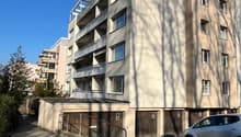 5-story building, beige exterior, multiple balconies, garage entrance, shadow of person and trees