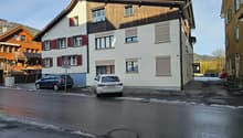 3 story house, white walls, brown roof, red shutters, cars parked