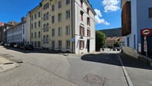 4 story building, yellow exterior, red window shutters, blue handicap parking sign, corner street, cars parked on the street
