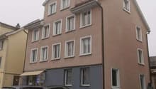 Three-story house with multiple windows, beige facade, awning, parking area